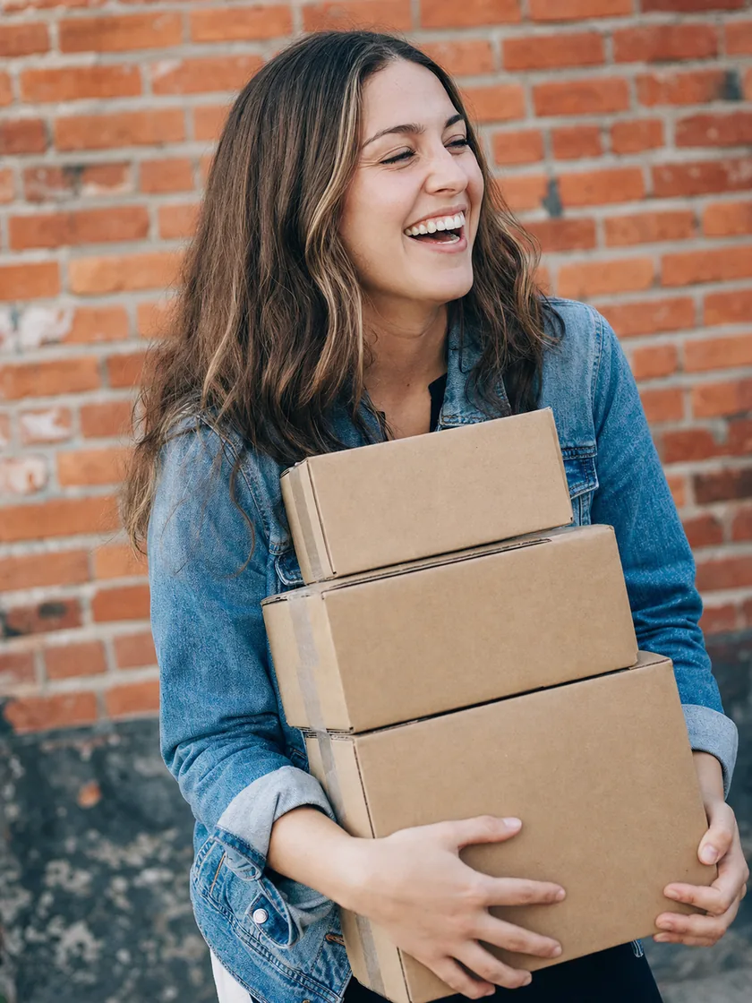 Smiling reseller carrying a stack of shipping boxes, ready to list inventory